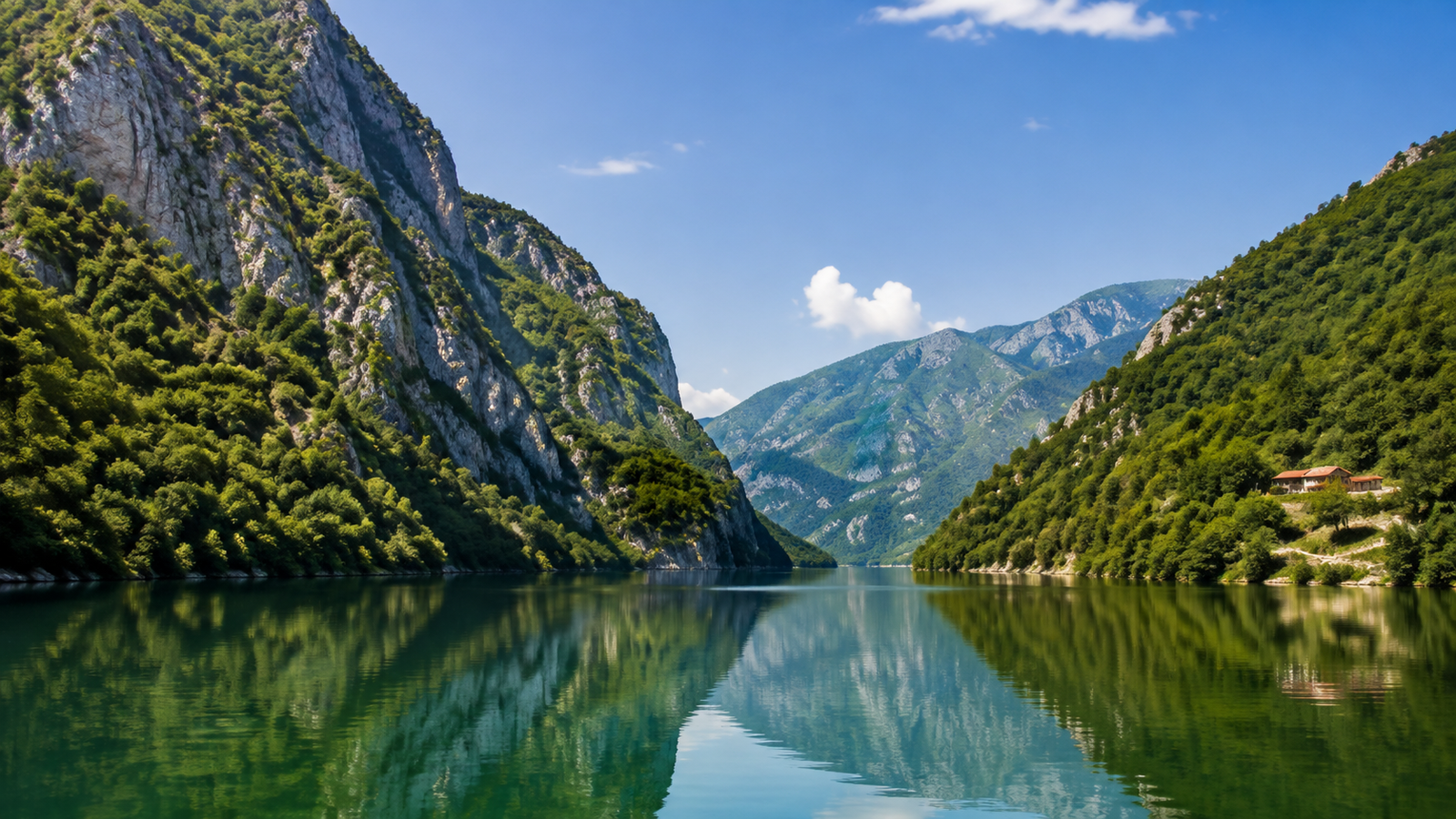 Boat crossing the emerald water of Lake Koman between high mountain walls